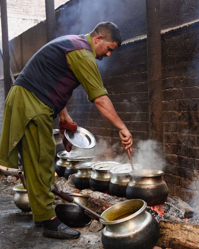 A cook stirring large pots over a wood fire